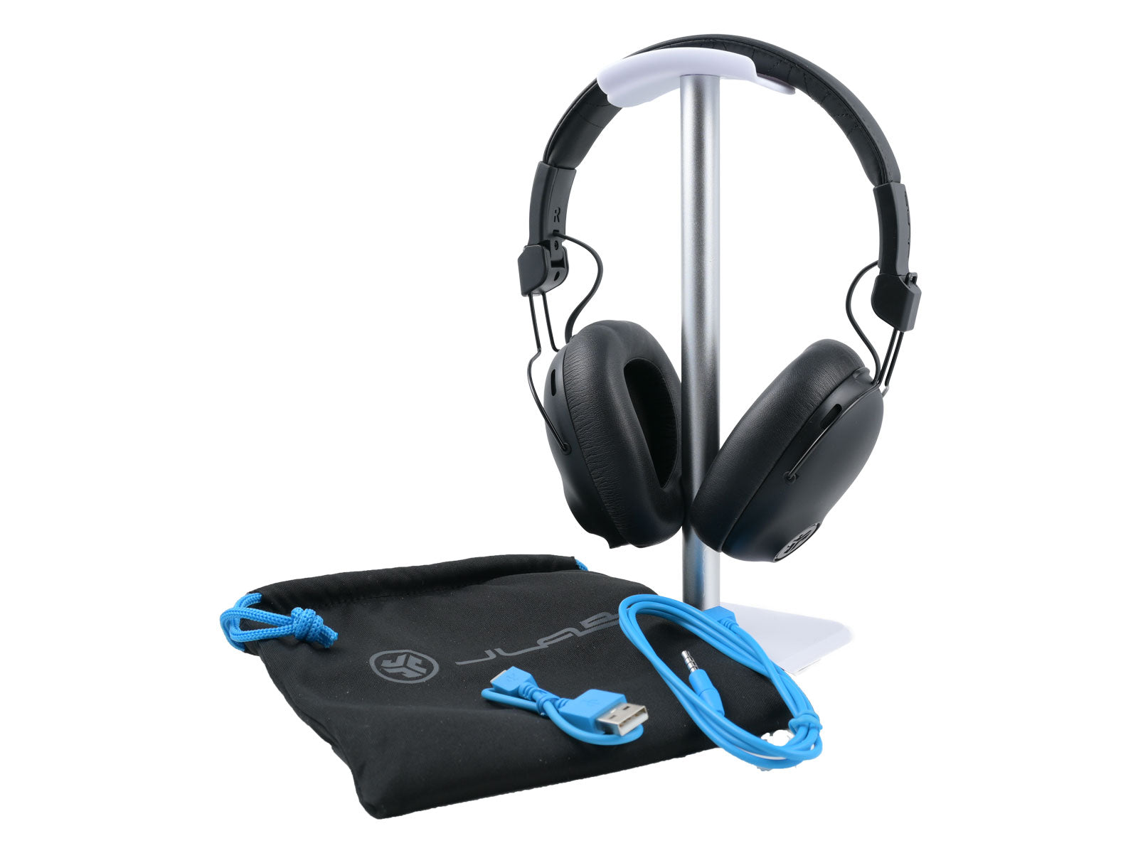 JLab Studio Pro ANC Wireless Over-Ear Kopfhörer Ein Paar schwarzer Over-Ear-Kopfhörer mit gepolsterten Ohrmuscheln und Kopfbügel aufrecht auf einem Ständer auf weißem Hintergrund, blaue Zubehörkabel und ein Beutel mit dem JLab Logo und einem blauen Zugband sind am Ständerfuß.