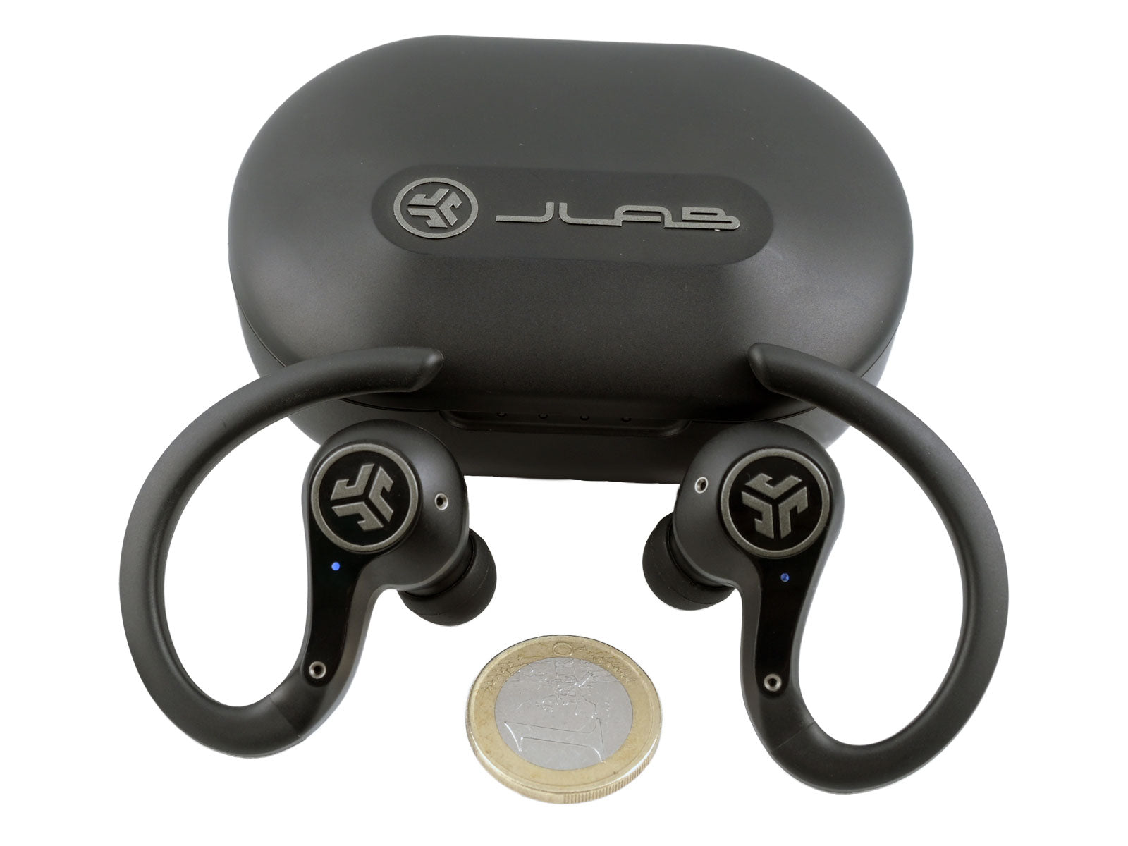 JLab Epic Air Sport ANC True Wireless Earbuds In-Ear Kopfhörer Schwarze kabellose Ohrhörer mit Ohrbügeln, platziert vor einem schwarzen Ladeetui mit der Aufschrift „JLab“, daneben eine Ein-Euro-Münze für den Größenvergleich auf weißem Hintergrund.