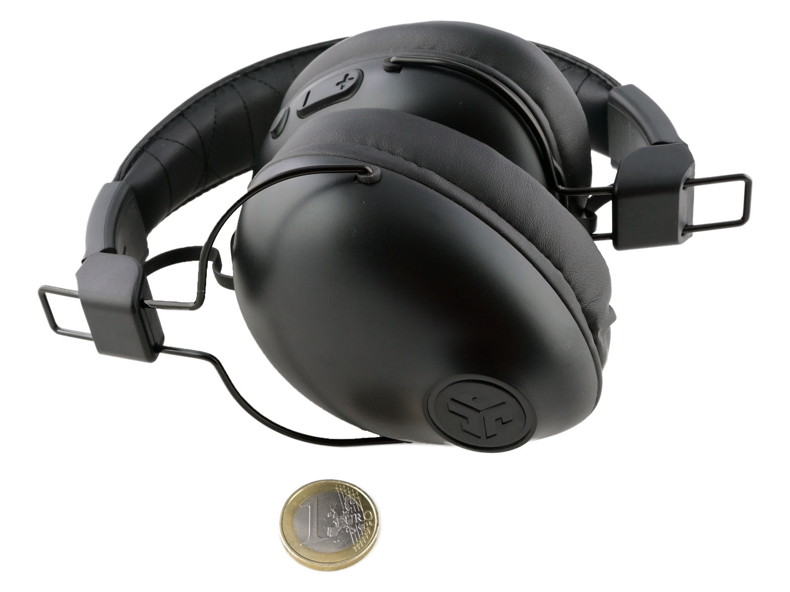 JLab Studio Pro Wireless Over-Ear Kopfhörer Over-Ear-Kopfhörer liegen auf weißem Hintergrund neben einer kleinen Münze, die ihre Größe verdeutlicht.