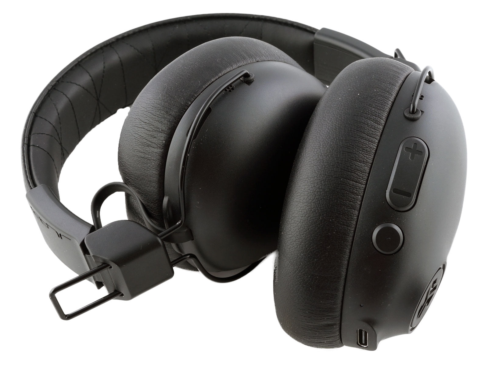 JLab Studio Pro ANC Wireless Over-Ear Kopfhörer Die schwarzen Over-Ear-Kopfhörer liegen zusammengeklappt da und zeigen Kissen und Kopfbügeldetails in minimalistischem Design. Der weiße Hintergrund betont ihre schlanke, kompakte Form.